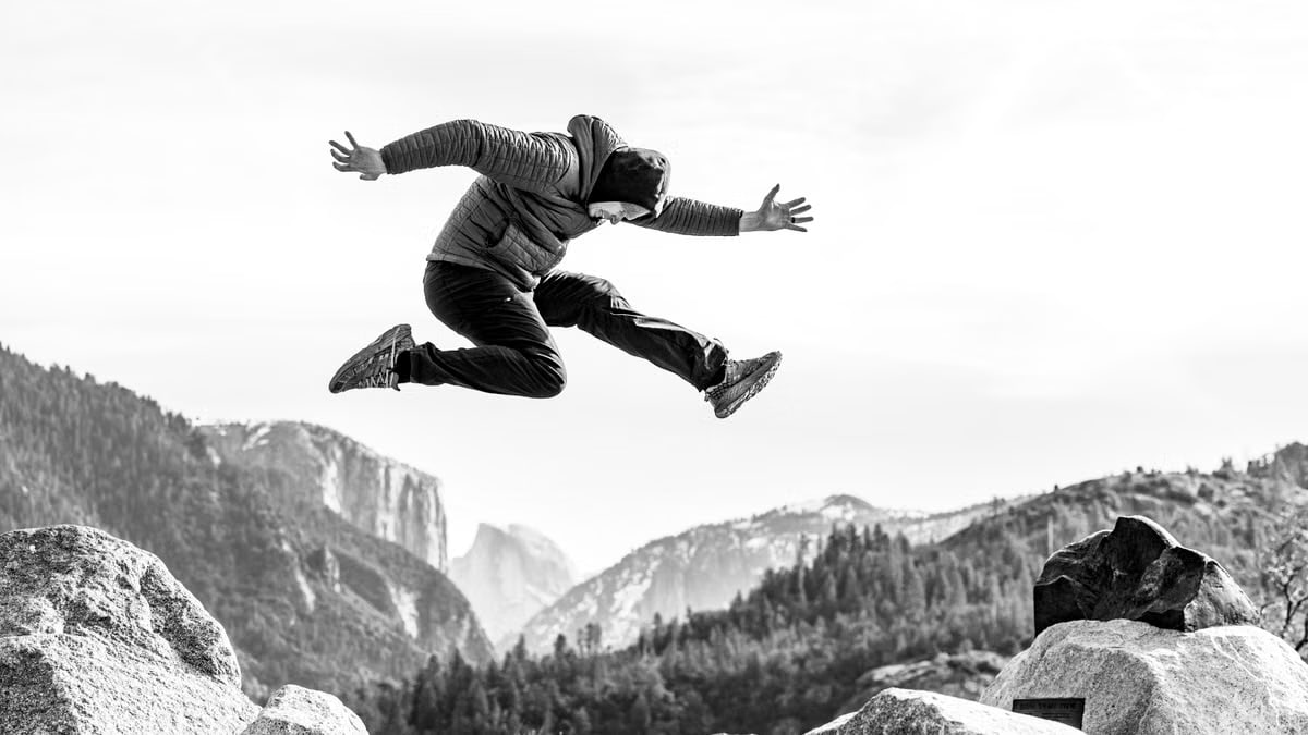 Black and white photo of a person jumping over rocks in Yosemite National Park, showcasing adventure and freedom.